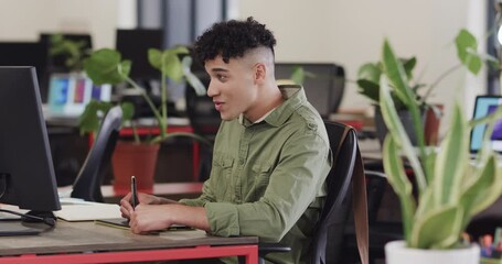 Wall Mural - happy biracial male creative using tablet and computer at casual office, in slow motion