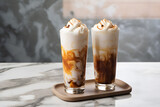 two tall glasses with warm coffee drink with cinnamon, whipped milk foam and caramel on a marble board. Generative AI technology