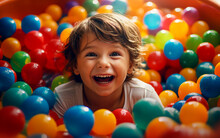 Cute And Smiling Child Has Fun And Jumps Into The Tub Full Of Colorful Balls. Happy And Smiling