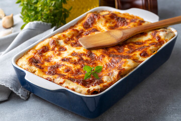 Portion of ground beef lasagna topped with melted cheese and garnished with fresh parsley served on a plate in close view for a menu