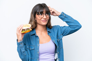 Canvas Print - Young caucasian woman holding a burger isolated on white background having doubts and with confuse face expression