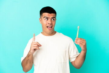 Wall Mural - Young handsome man brushing teeth over isolated blue background thinking an idea pointing the finger up