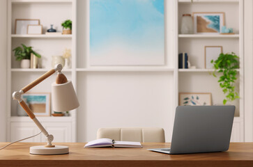 Poster - Interior design. Cosy workplace with laptop and lamp on wooden table near abstract picture between shelves