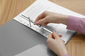 Wall Mural - Woman fixing folder with punched pockets at wooden table, closeup