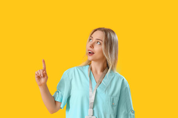 Wall Mural - Female medical intern pointing at something on yellow background