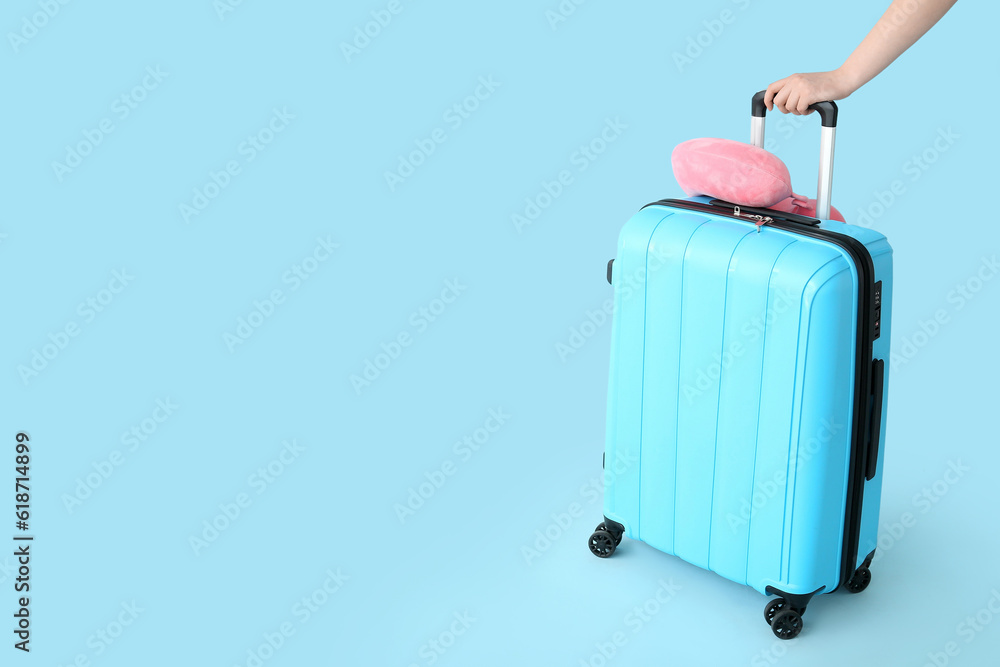 Female hand with suitcase and travel cushion on blue background. Travel concept
