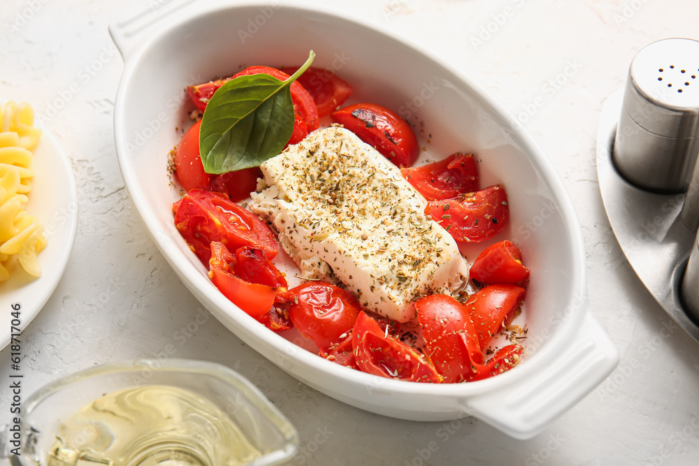 Baking dish with tasty tomatoes and feta cheese on light background