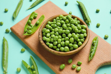 Bowl and wooden board with fresh green peas on turquoise background