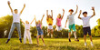 © Studio Romantic - Children having fun in the park on a sunny summer day. Group of cheerful kid friends boys girls enjoying summertime, playing on green grass outdoors, feeling free and happy, jumping up to clear sky