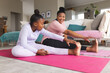 © Wavebreak Media - Happy african american mother and daughter doing yoga and stretching in living room
