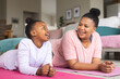 © Wavebreak Media - Happy african american mother and daughter lying on yoga mats and talking in living room