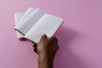 Poster - Hand of biracial man holding notebook over notebooks with copy space on pink background