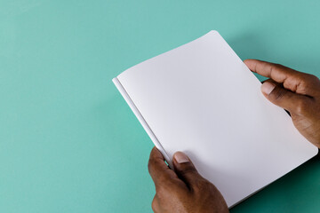 Canvas Print - Hands of biracial man holding book with copy space on green background