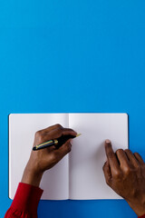 Wall Mural - Hands of biracial man holding pen and writing in notebook with copy space on blue background