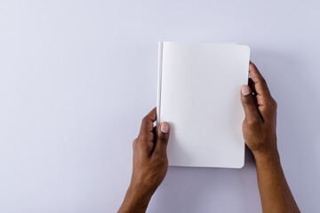 Canvas Print - Hands of biracial man holding book with copy space on grey background