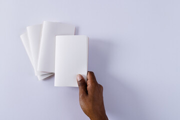 Poster - Hand of biracial man holding notebook over notebooks with copy space on white background