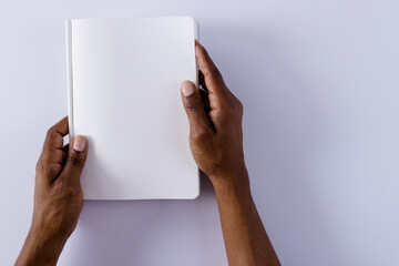 Canvas Print - Hands of biracial man holding book with copy space on grey background