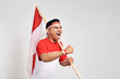 © Bangun Stock Photo - Excited young Asian man standing holding Indonesian flag with raised hands while Celebrate Indonesia independence day on 17 August isolated over white background