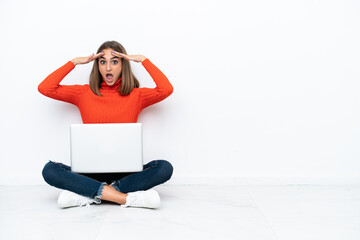 Wall Mural - Young caucasian woman sitting on the floor with a laptop with surprise expression