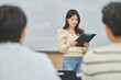 © TEAM PRE-LIGHT - A female college student in Asia is standing in front of a lecture hall at a university in South Korea, giving a presentation and lecture. The male students are sitting in front of her