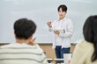 © TEAM PRE-LIGHT - An Asian young man is standing in front of a lecture hall at a university in South Korea, giving a presentation or lecture. In front of him are male and female students.