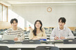© TEAM PRE-LIGHT - Three young Asian college students, both male and female, are in a classroom in South Korea where they are either teaching or studying