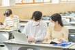 © TEAM PRE-LIGHT - In a higher education classroom in South Korea, young university students wearing masks are listening to a lecture, studying, and talking. A woman and a man are in the background