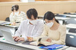 © TEAM PRE-LIGHT - In a higher education classroom in South Korea, young university students wearing masks are listening to a lecture, studying, and talking. A woman and a man are in the background