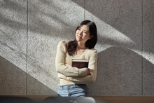 A Young Female College Student Model Leaning Against The Wall Of A University Classroom In A Light-filled Room In South Korea, Asia.  
