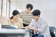 © TEAM PRE-LIGHT - Three young male and female college students models sitting or standing at desks in a university classroom in South Korea, Asia, talking or having a discussion