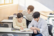 © TEAM PRE-LIGHT - Three young male and female college students models sitting or standing at desks in a university classroom in South Korea, Asia, talking or having a discussion