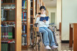 © TEAM PRE-LIGHT - A young female college student with a disability is reading a book in a wheelchair at a university library in South Korea