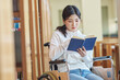 © TEAM PRE-LIGHT - A young female college student with a disability is reading a book in a wheelchair at a university library in South Korea