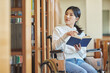 © TEAM PRE-LIGHT - A young female college student with a disability is reading a book in a wheelchair at a university library in South Korea