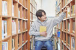 © TEAM PRE-LIGHT - Asia South Korea university library bookcase in a wheelchair looking for a book on the shelf, physically handicapped young disabled male college student model