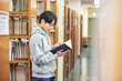 © TEAM PRE-LIGHT - A young man attending college is browsing and reading books on the shelves with different expressions in his university library in South Korea, Asia.