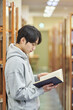 © TEAM PRE-LIGHT - A young man attending college is browsing and reading books on the shelves with different expressions in his university library in South Korea, Asia.