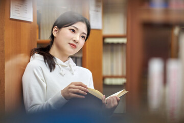 A female college student is reading a book in a university library in South Korea, Asia, with various expressions on her face as she browses the books on the shelves