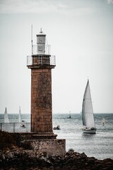 Canvas Print - Sailboat near a lighthouse, peacefully gliding through the calm waters