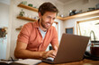 © HockleyMedia/peopleimages.com - Networking, laptop and remote work, happy man at kitchen counter with email, social media post or research for job. Technology, writer or freelancer on internet typing blog or online article at home.