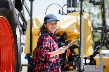 Sticker - Woman farmer with a digital tablet on the background of an agricultural tractors