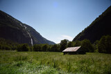 Fototapeta Morze - Mountain landscape with waterfall and wooden house in the middle of the valley