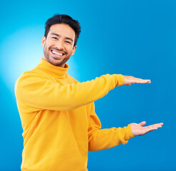 Wall Mural - Presenting, advertising and portrait of Asian man on blue background for news, showing and copy space. Studio, branding and face of male person with hand gesture for promotion, deal and presentation