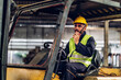 © kanpisut - Man worker at forklift driver happy working in industry factory logistic ship. Man forklift driver in warehouse area. Forklift driver sitting in vehicle in warehouse.