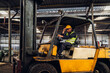 © kanpisut - Man worker at forklift driver happy working in industry factory logistic ship. Man forklift driver in warehouse area. Forklift driver sitting in vehicle in warehouse.