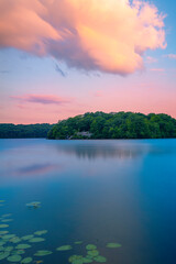 Wall Mural - Sunset and dramatic cloudscape over the lake with green forest, water lilies, and reflections at Lincoln State Park in Providence, Rhode Island