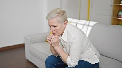 Poster - Middle age grey-haired woman sitting on sofa with serious expression at home