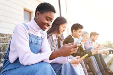 Technology Addicted smiling group of cheerful students using mobiles. They check multimedia in their phones happy and do not look at each other. They laugh outdoors the college