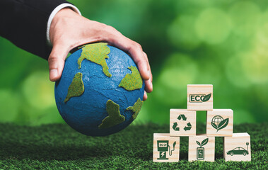 Businessman hand holding wooden cube with eco symbol and paper globe on fertile soil background. Environmental awareness and sustainable energy. Clean and renewable energy for greener ecology. Alter