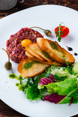 Canvas Print - Fresh beef tartare with raw egg, fried bread, capers, French mustard, tomatoes, salad and sauce.